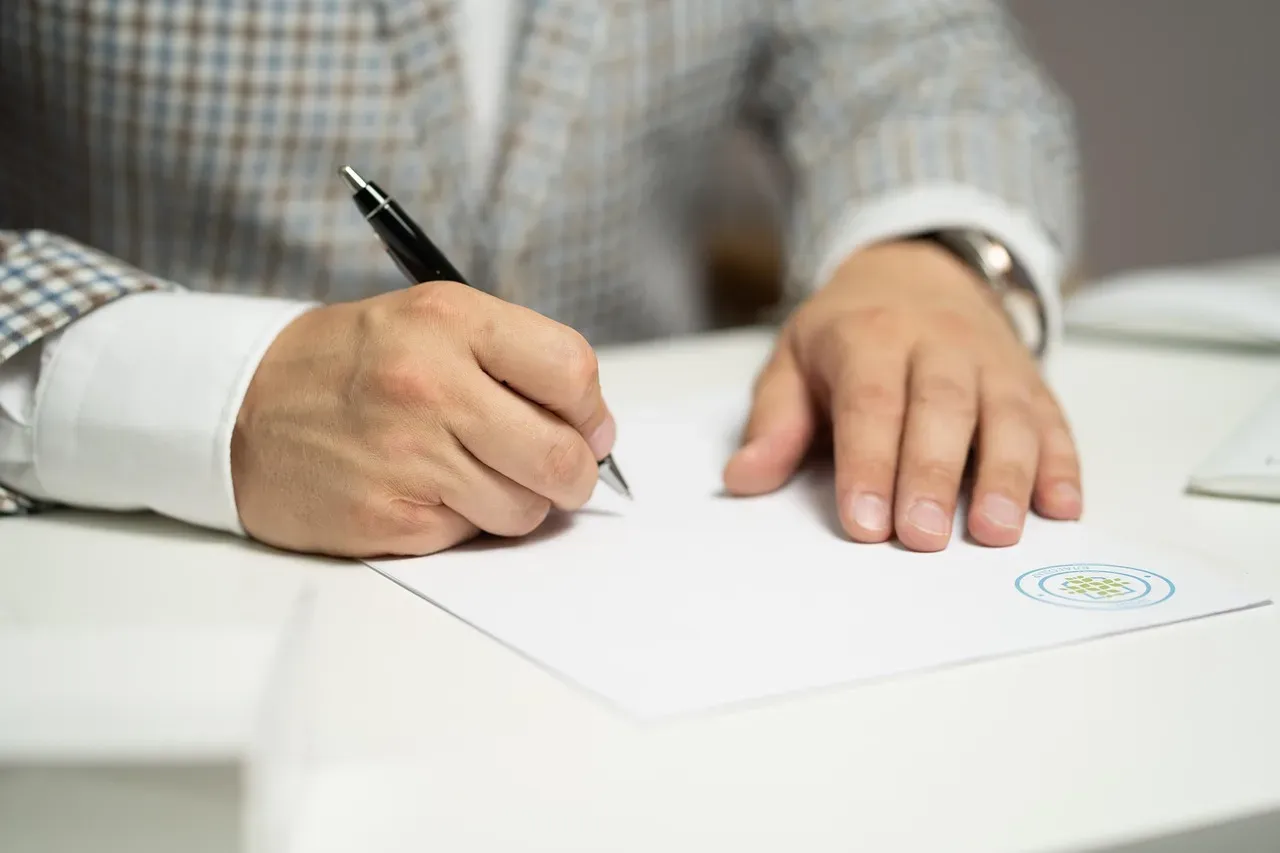 Mains d'un homme écrivant avec un stylo sur une feuille blanche de démarches.
